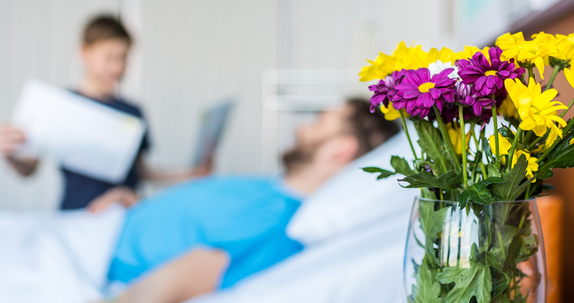 Bild im Vordergrund Blumenstrauß im Hintergrund Patient und Pflegerin